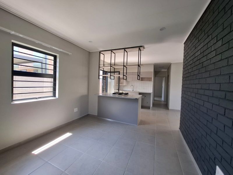 Modern open-plan living and kitchen area featuring a central island with gas hob, suspended shelving, and a striking dark brick feature wall.