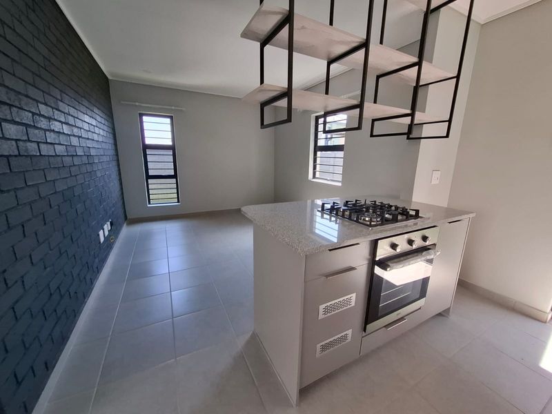 Modern kitchen featuring a central island with gas hob and oven, complemented by a striking dark brick feature wall and contemporary suspended shelving.