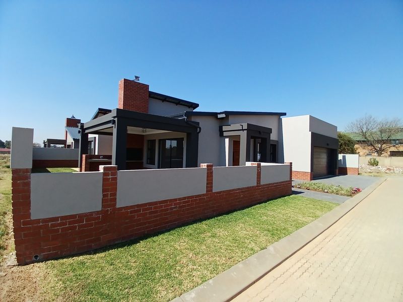 Modern single-story house featuring a brick and plaster facade, covered patio, integrated garage, and a well-maintained front lawn with a brick boundary wall.