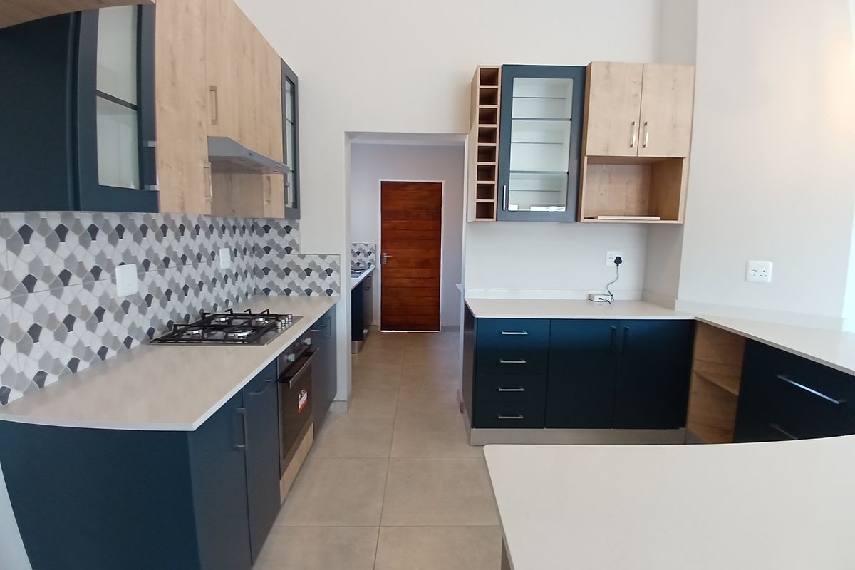 Modern kitchen featuring two-tone cabinetry, stone countertops, a gas hob, built-in oven, and a decorative tiled backsplash with neutral floor tiles.