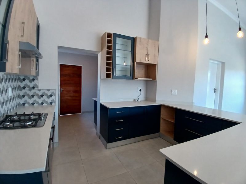 Modern kitchen featuring two-tone cabinetry, stone countertops, gas hob, extractor fan, and stylish tiled backsplash in an open-plan layout.