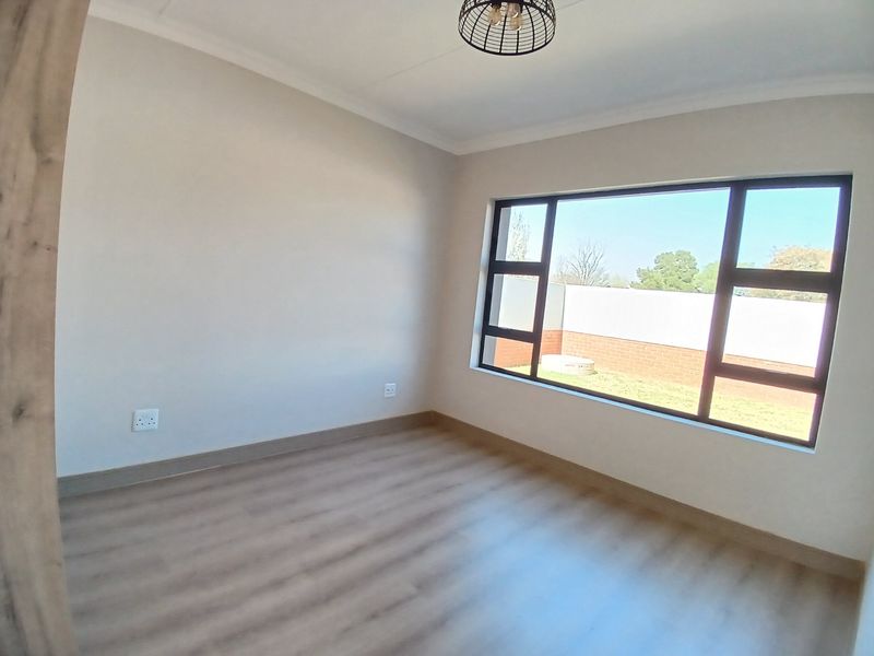 A bright, empty bedroom featuring modern laminate flooring, neutral walls, and a large window providing natural light and a view of the rear garden.