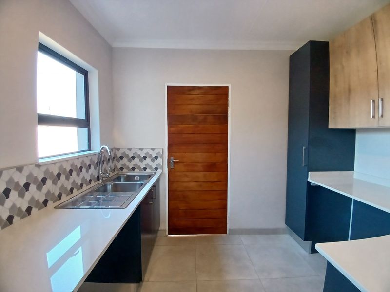 Modern kitchen featuring sleek two-tone cabinetry, white quartz countertops, a stainless steel double sink, and a decorative tiled backsplash.