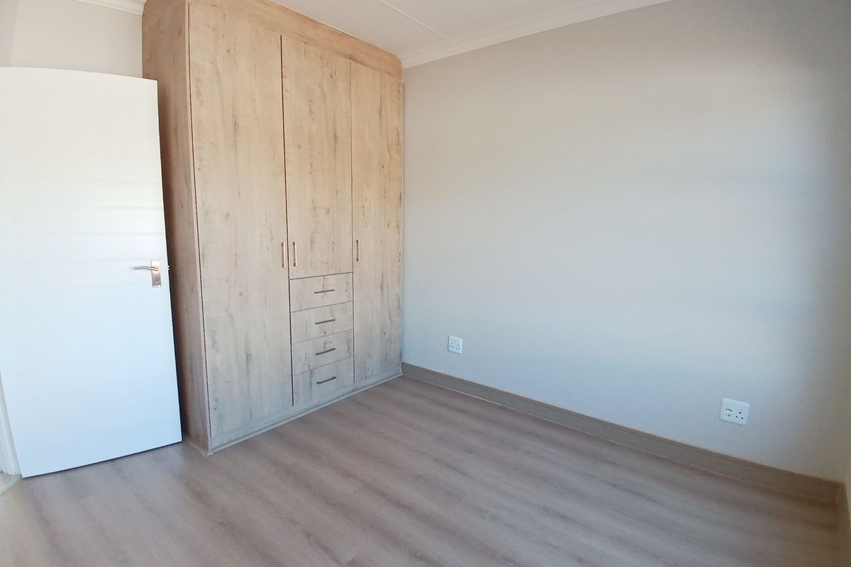 A clean, empty bedroom featuring modern light wood-look laminate flooring and a matching built-in wardrobe with integrated drawers.
