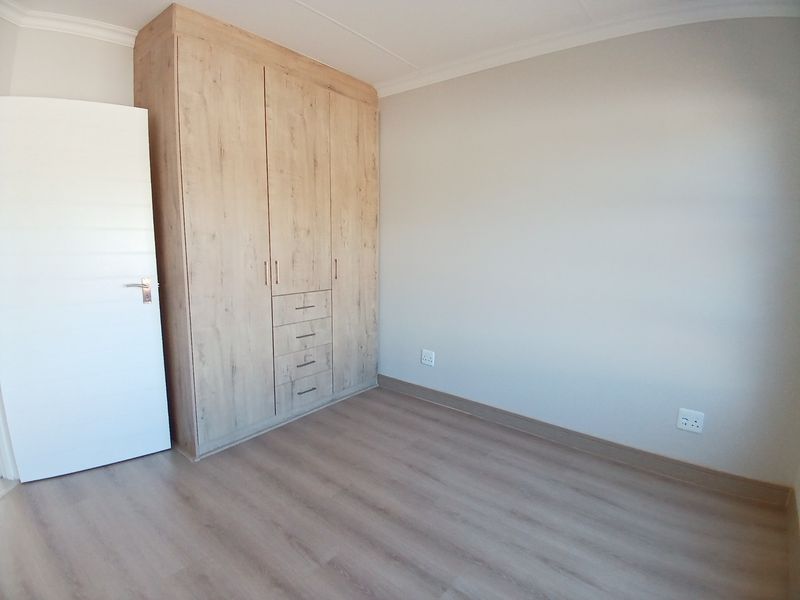 A clean, empty bedroom featuring modern light wood-look laminate flooring and a matching built-in wardrobe with integrated drawers.