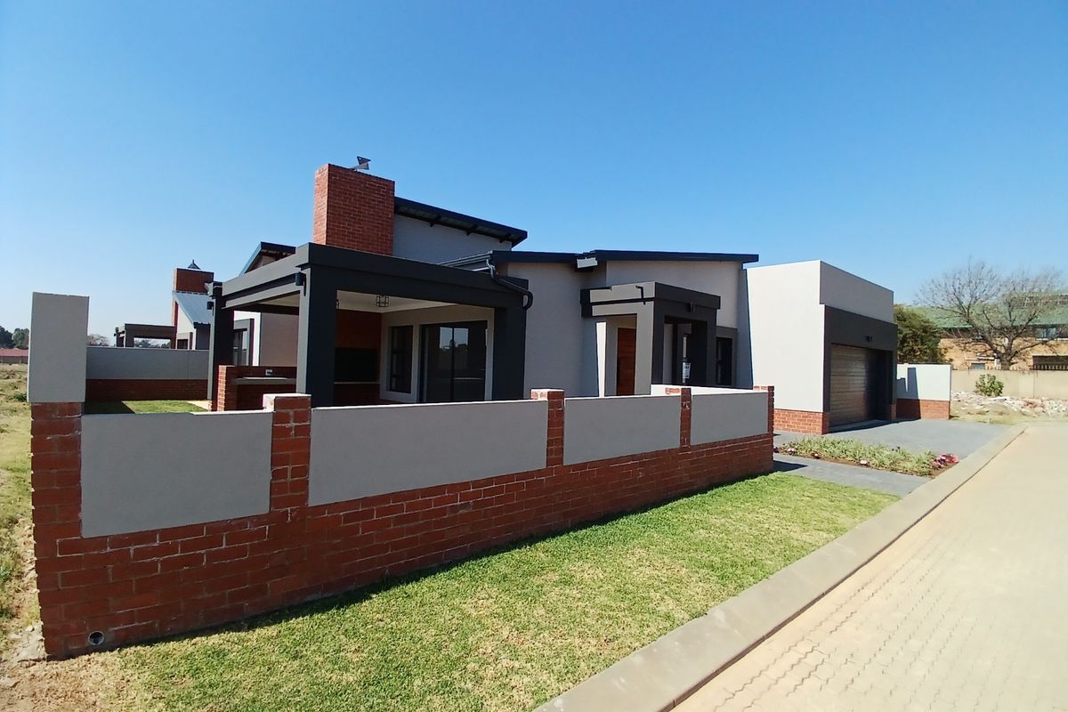 Modern single-story house featuring a brick and plaster facade, covered patio, integrated garage, and a well-maintained front lawn with a brick boundary wall.