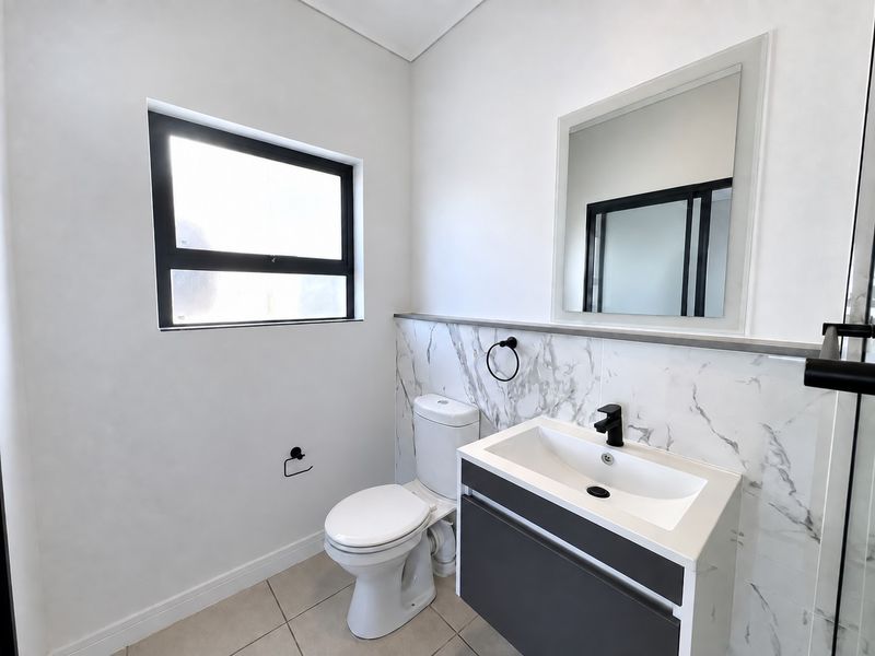 Modern bathroom featuring a sleek vanity with a black mixer tap, marble-look wall tiling, a contemporary toilet, and a framed mirror.