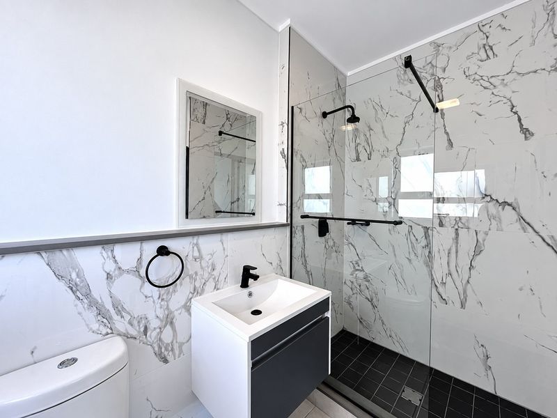 Modern bathroom featuring marble-look wall tiles, a spacious walk-in shower with black fixtures, and a sleek wall-mounted vanity.