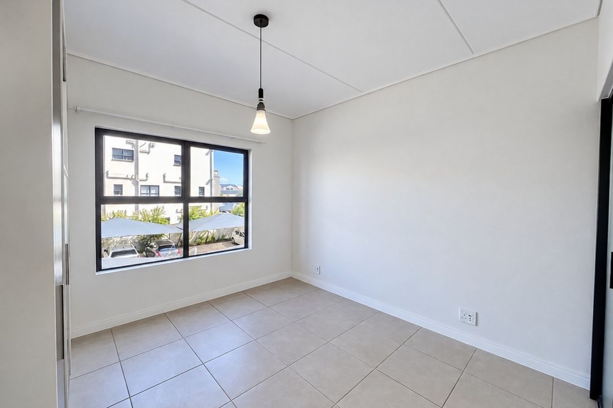 A bright, empty bedroom featuring neutral tiled flooring, a modern pendant light, and a large window with black frames.