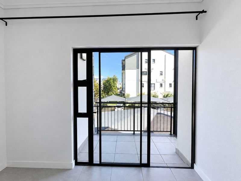 A bright, modern balcony featuring tiled flooring, a black metal balustrade, and large sliding glass doors providing access to the outdoor space.