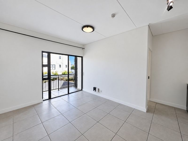 A bright, empty living area featuring neutral tiled flooring and a sliding glass door providing direct access to a private balcony.