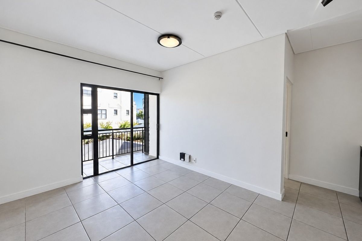 A bright, empty living area featuring neutral tiled flooring and a sliding glass door providing direct access to a private balcony.