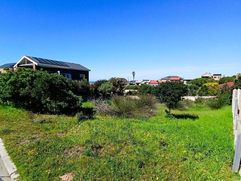 A view of a vacant residential plot featuring natural grass coverage and surrounding neighborhood infrastructure.