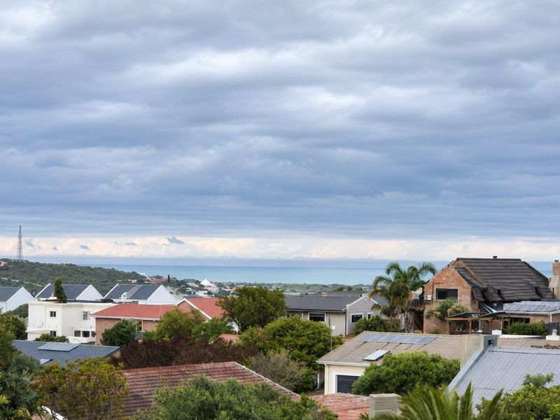 A scenic elevated view overlooking a residential neighborhood with a distant coastal horizon under a cloudy sky.