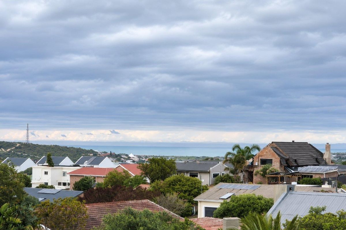 A scenic elevated view overlooking a residential neighborhood with a distant coastal horizon under a cloudy sky.