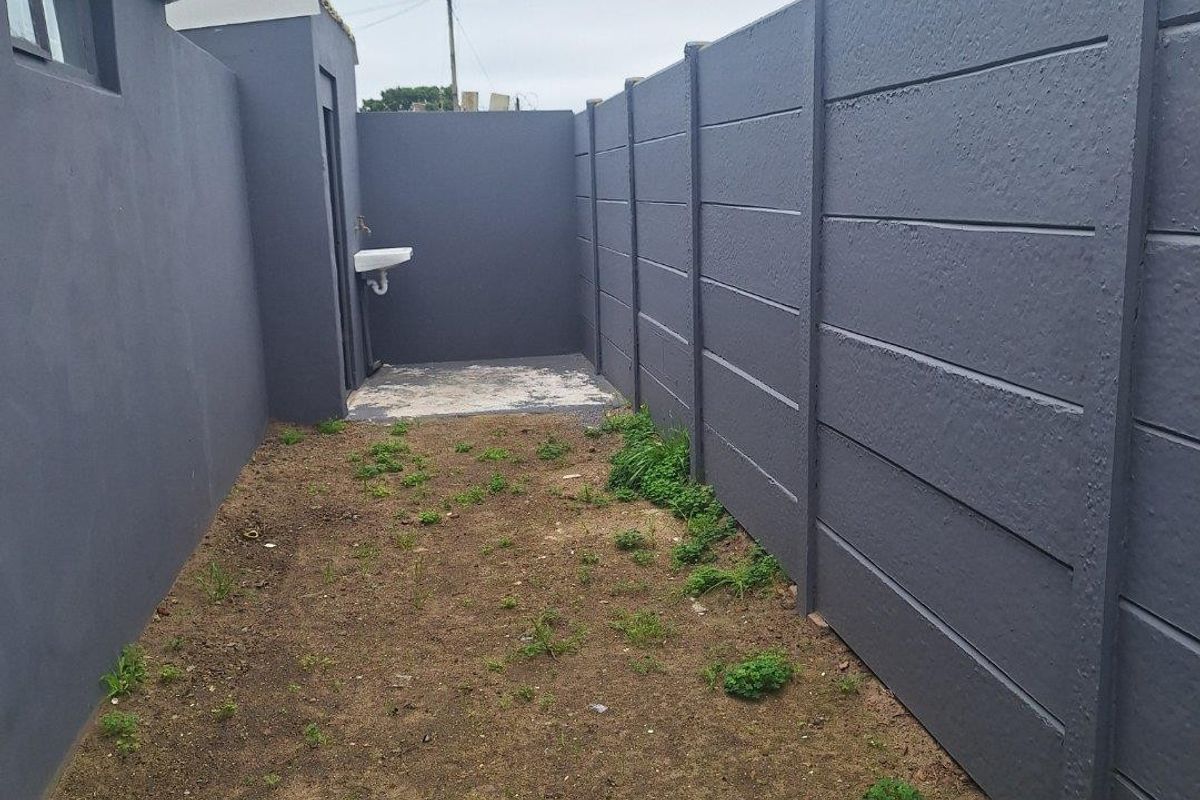 A narrow rear exterior area featuring a painted precast concrete boundary wall, an external basin, and an unlandscaped ground surface.