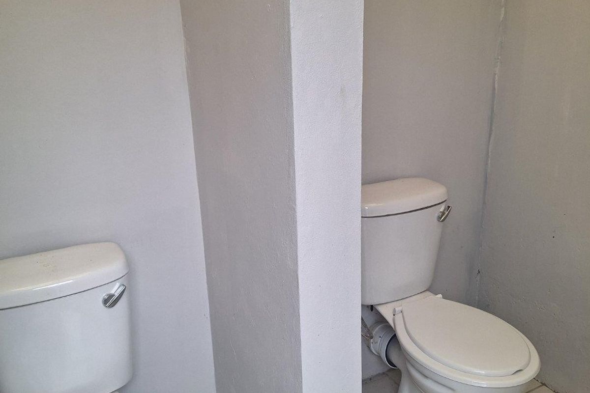 A commercial bathroom facility featuring two toilets separated by a central partition wall with tiled flooring.