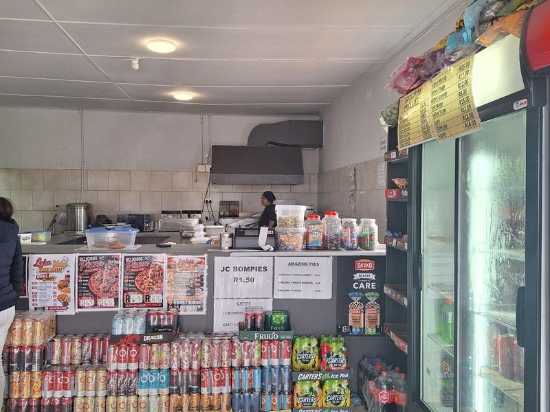 A commercial kitchen service area featuring a service counter, tiled splashback, extractor fan, and a large glass-fronted display refrigerator for beverages.