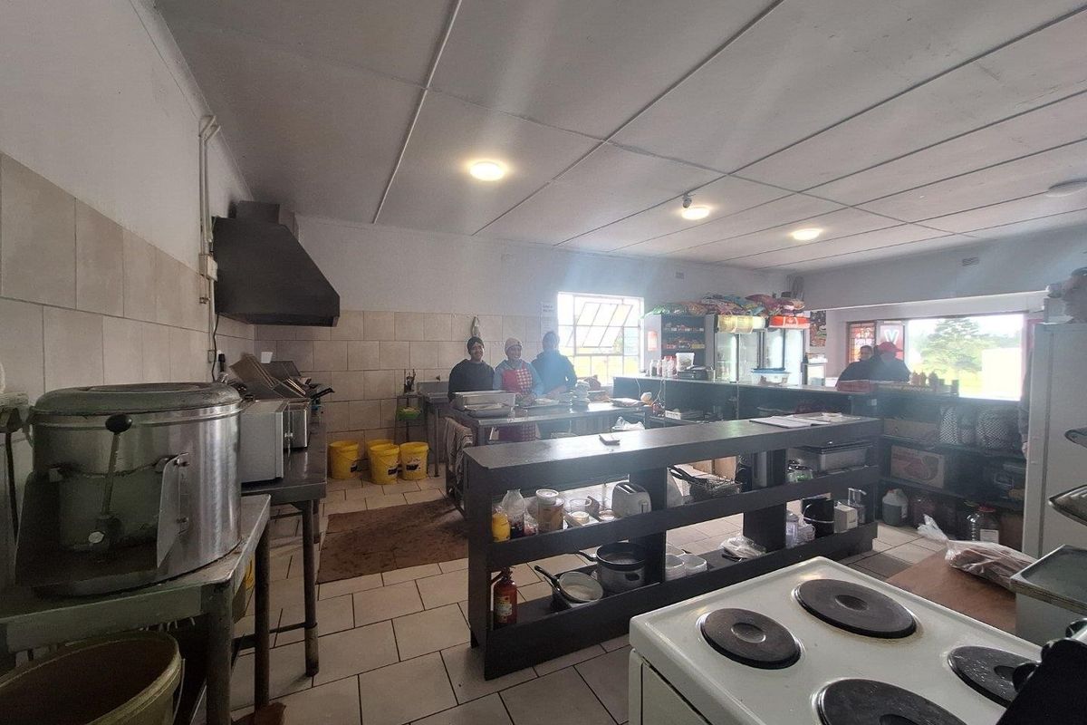 A functional commercial kitchen space featuring tiled flooring, wall splashbacks, an extractor fan, and built-in shelving units for storage.