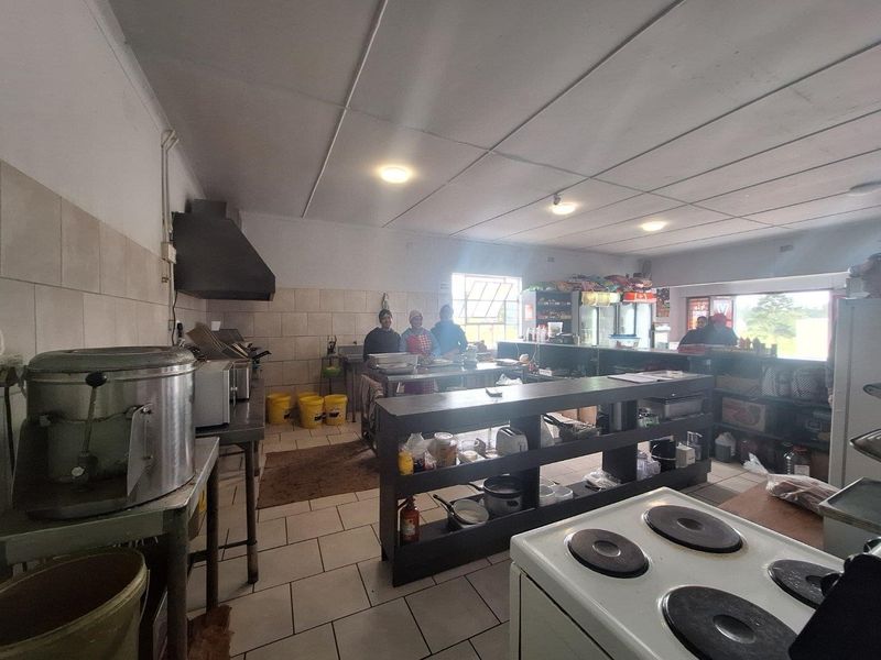 A functional commercial kitchen space featuring tiled flooring, wall splashbacks, an extractor fan, and built-in shelving units for storage.