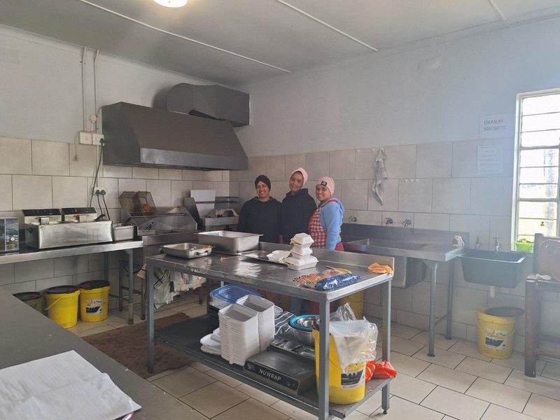 A functional commercial kitchen featuring stainless steel prep stations, a commercial-grade extractor hood, tiled walls, and a double-basin sink setup.