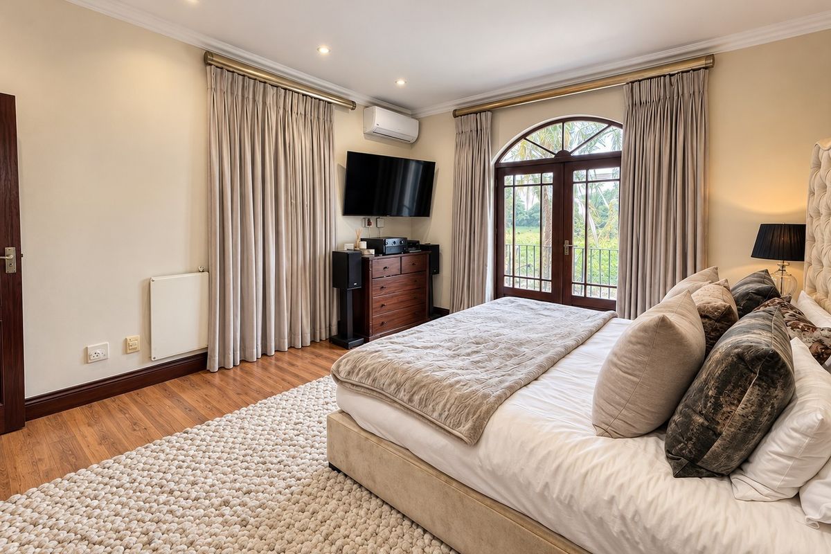 A well-maintained bedroom featuring laminate flooring, recessed lighting, a wall-mounted air conditioning unit, and arched double doors leading to an outdoor space.