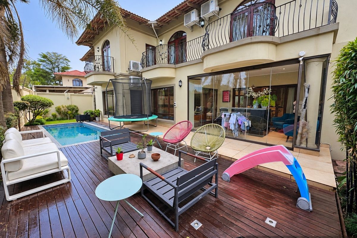 Rear exterior view featuring a swimming pool, timber decking, tiled patio, and a two-story residence with balcony access.