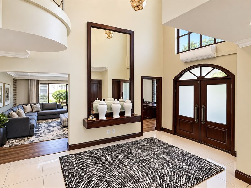 Spacious double-volume entrance hall featuring elegant double doors, polished tile flooring, and a mezzanine overlook, creating a grand and welcoming first impression.