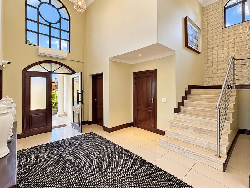 Spacious double-volume entrance hall featuring an arched front door, elegant stone staircase with stainless steel balustrade, and high-quality tiled flooring.