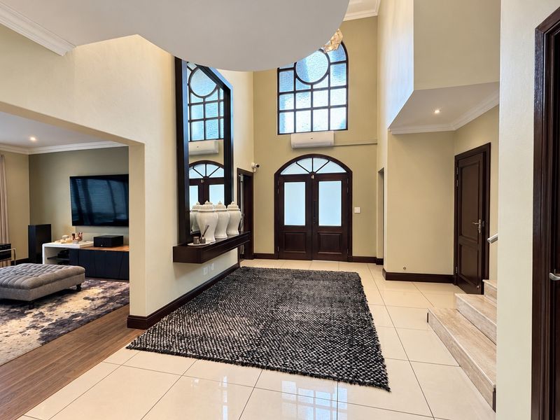Spacious double-volume entrance hall featuring tiled flooring, elegant arch-top windows, and a grand staircase, creating a bright and welcoming foyer.