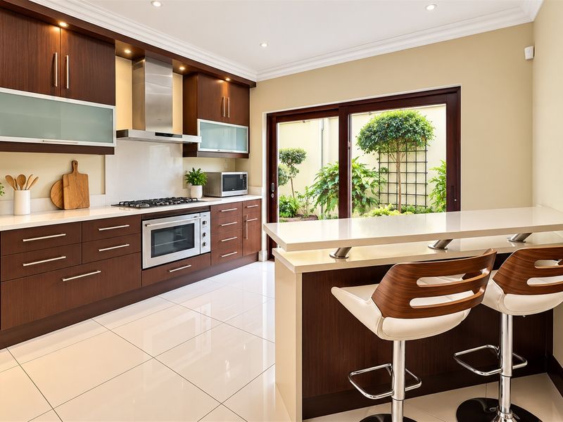 Modern kitchen featuring dark wood cabinetry, stone countertops, integrated appliances, a breakfast bar, and direct access to a private courtyard through sliding glass doors.