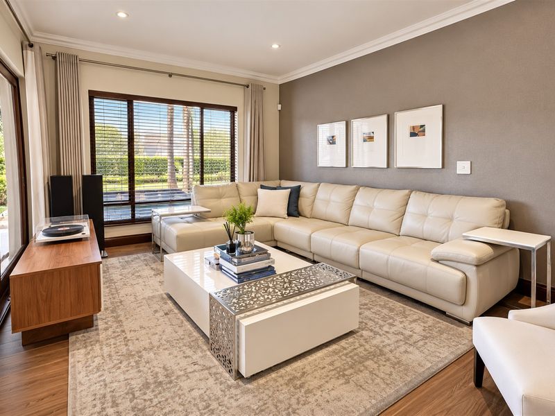 A well-maintained living room featuring timber flooring, recessed downlights, crown molding, and a large sliding glass door providing natural light and garden access.