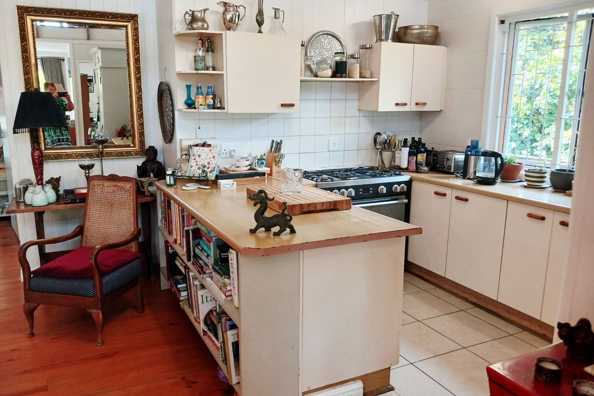 A functional kitchen featuring timber cabinetry, a gas cooktop, built-in oven, and a central timber island, with a mix of timber and tiled flooring.