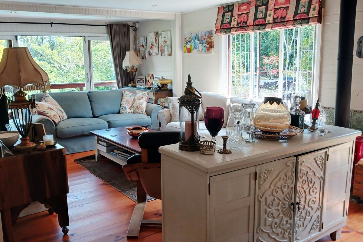 A bright living room featuring warm hardwood flooring, a wood-burning stove, and large windows that provide ample natural light and garden views.