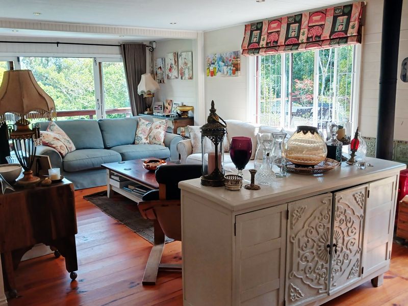 A bright living room featuring warm hardwood flooring, a wood-burning stove, and large windows that provide ample natural light and garden views.