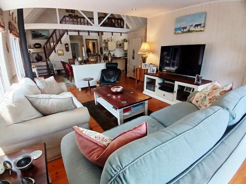 Spacious open-plan living area featuring exposed timber beams, a wood-burning stove, and a mezzanine level with a timber staircase.