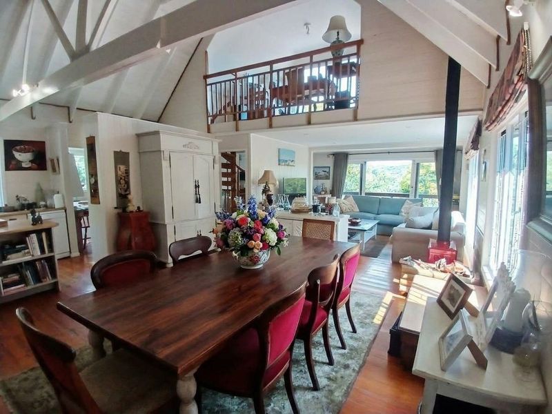 Spacious open-plan living and dining area featuring vaulted ceilings with exposed timber beams, a mezzanine level, and a cozy wood-burning fireplace.