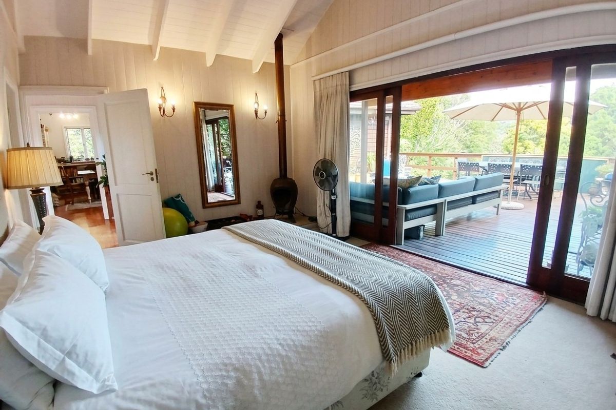 Spacious bedroom featuring a vaulted ceiling with exposed beams, a cozy wood-burning fireplace, and large sliding doors opening onto a private timber deck.