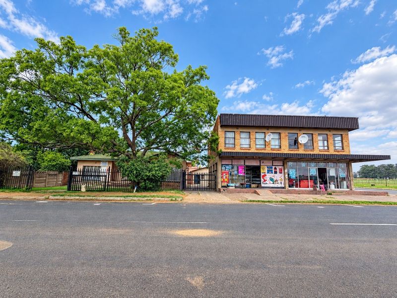 Street-facing view of a commercial property featuring a brick facade, storefront glazing, and secure perimeter fencing with a large mature tree.