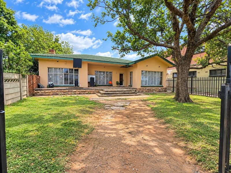 Rear view of the commercial property featuring a tiled roof, stone-clad patio, and a spacious garden area with established trees and secure perimeter fencing.