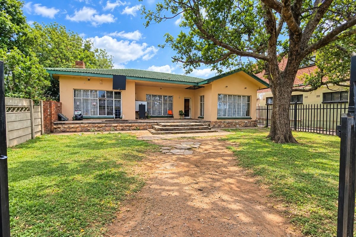 Rear view of the commercial property featuring a tiled roof, stone-clad patio, and a spacious garden area with established trees and secure perimeter fencing.