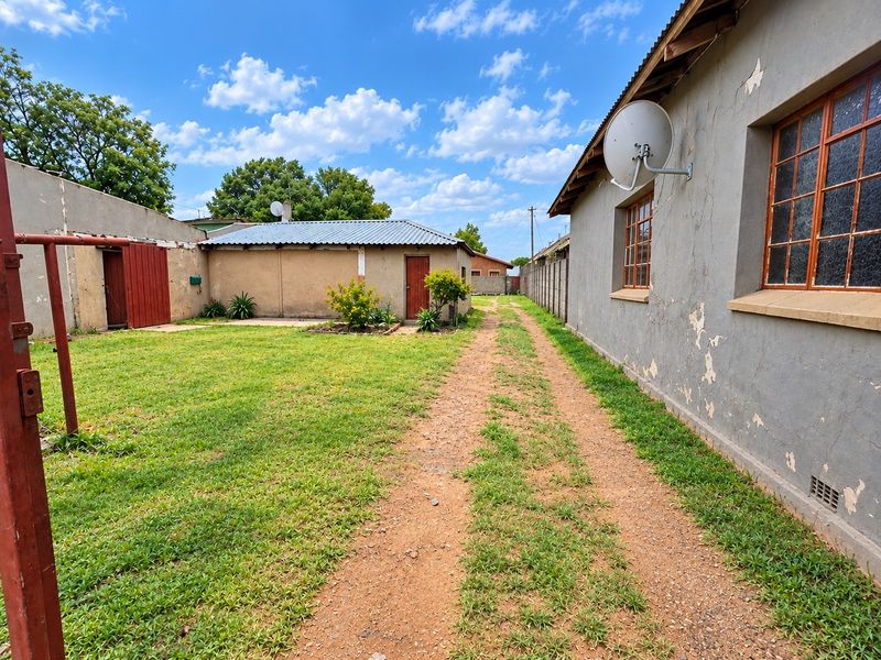 Rear exterior view of the commercial property featuring a gravel driveway, lawn area, and outbuilding with a metal roof and perimeter walling.
