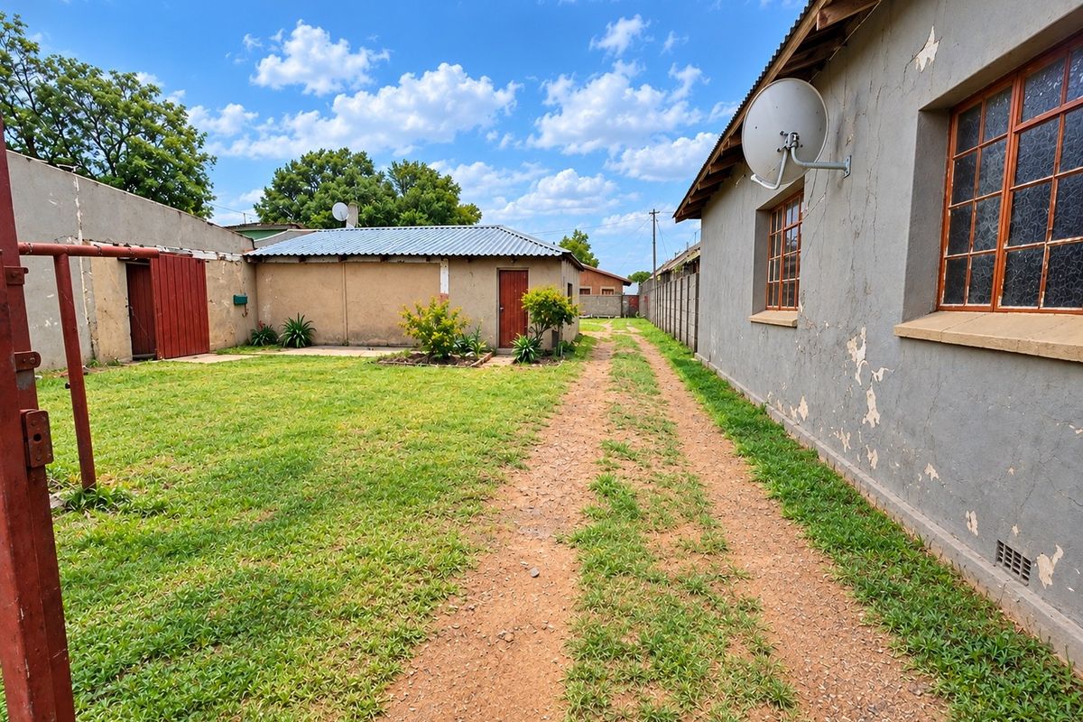Rear exterior view of the commercial property featuring a gravel driveway, lawn area, and outbuilding with a metal roof and perimeter walling.