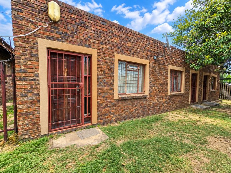 Exterior view of a commercial property featuring face brick construction, security gates, and steel-framed windows along a grassed area.