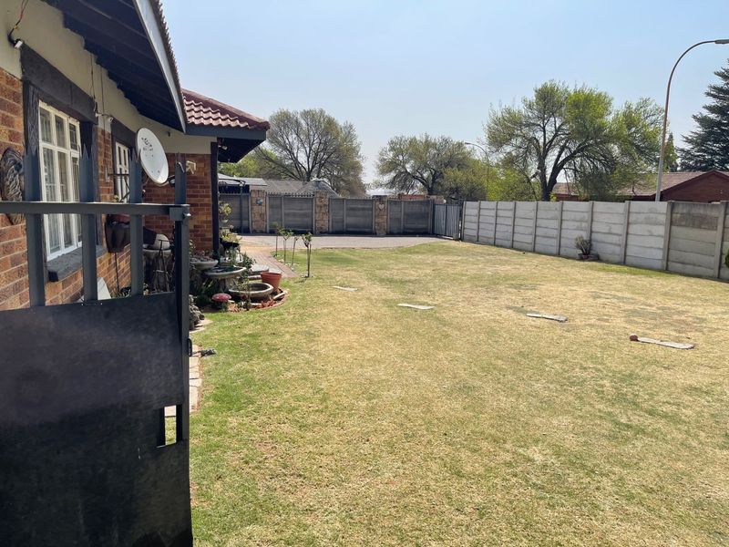 A spacious rear garden featuring a lawn, paved driveway area, and secure precast concrete boundary walls.