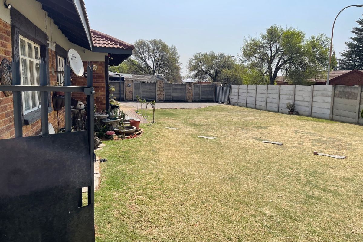 A spacious rear garden featuring a lawn, paved driveway area, and secure precast concrete boundary walls.