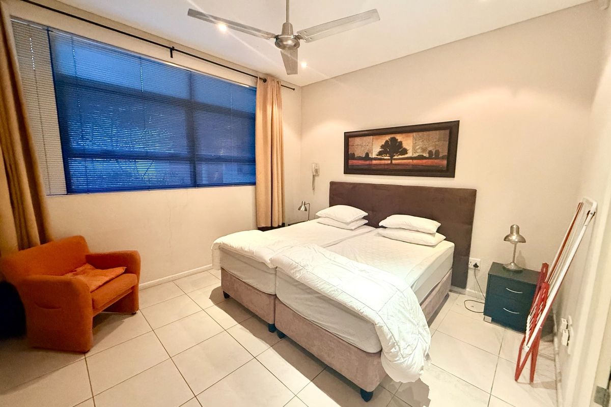 A functional bedroom featuring tiled flooring, a ceiling fan, and a large window with blinds, providing a neutral space ready for personalization.