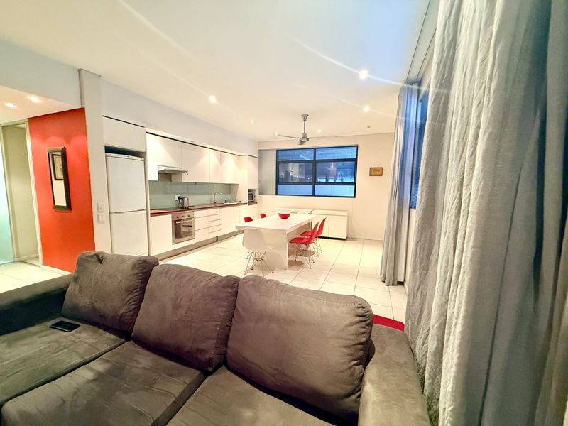 Open-plan living and kitchen area featuring modern white cabinetry, integrated appliances, tiled flooring, and recessed lighting, creating a functional and bright living space.