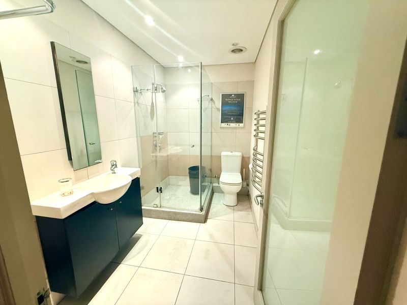 Modern bathroom featuring a vanity with basin, glass-enclosed shower, toilet, and a heated towel rail, finished with neutral floor and wall tiling.