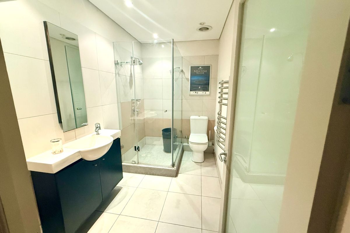Modern bathroom featuring a vanity with basin, glass-enclosed shower, toilet, and a heated towel rail, finished with neutral floor and wall tiling.